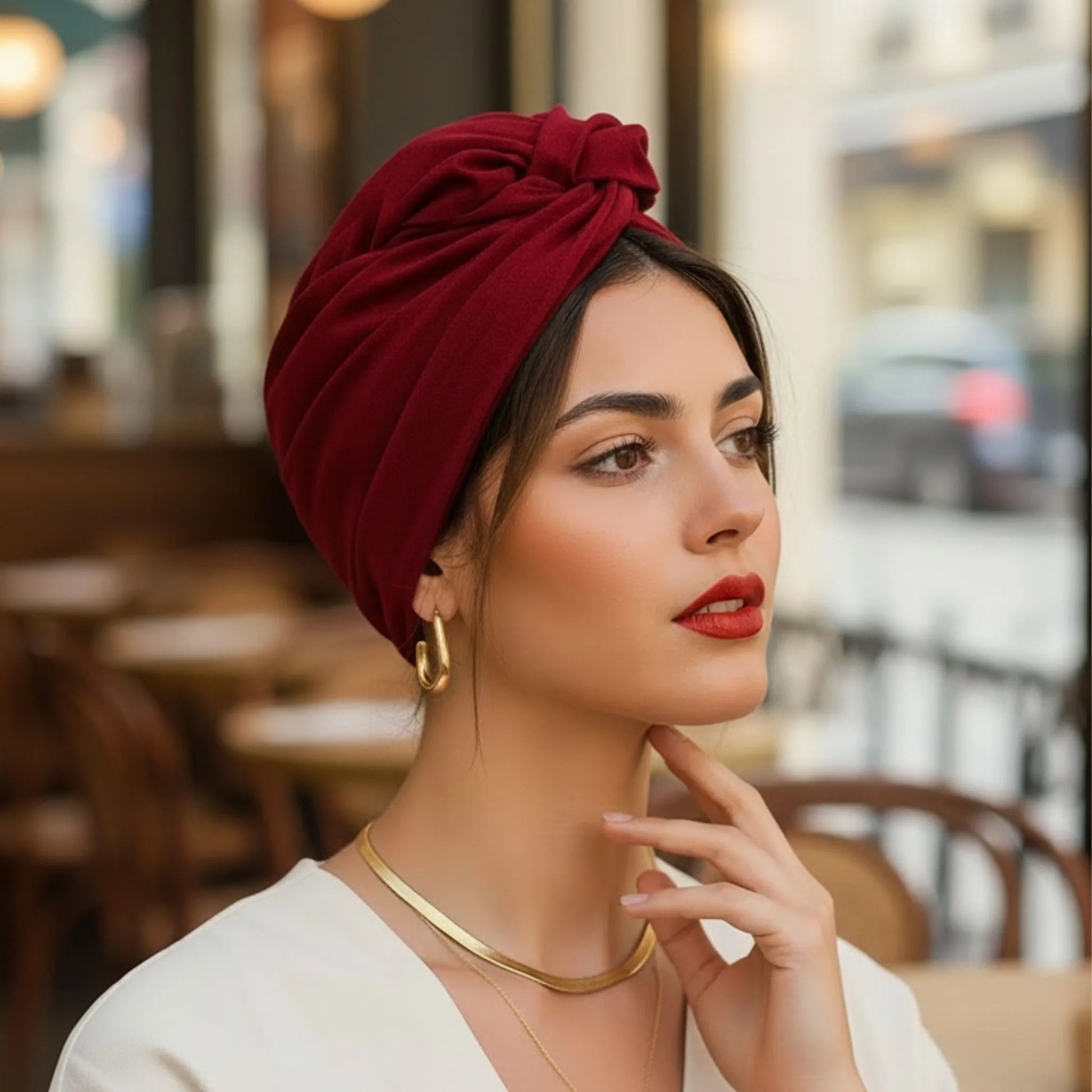 Mujer con turbante cubano burdeos de algodón disfrutando de un momento en una cafetería.